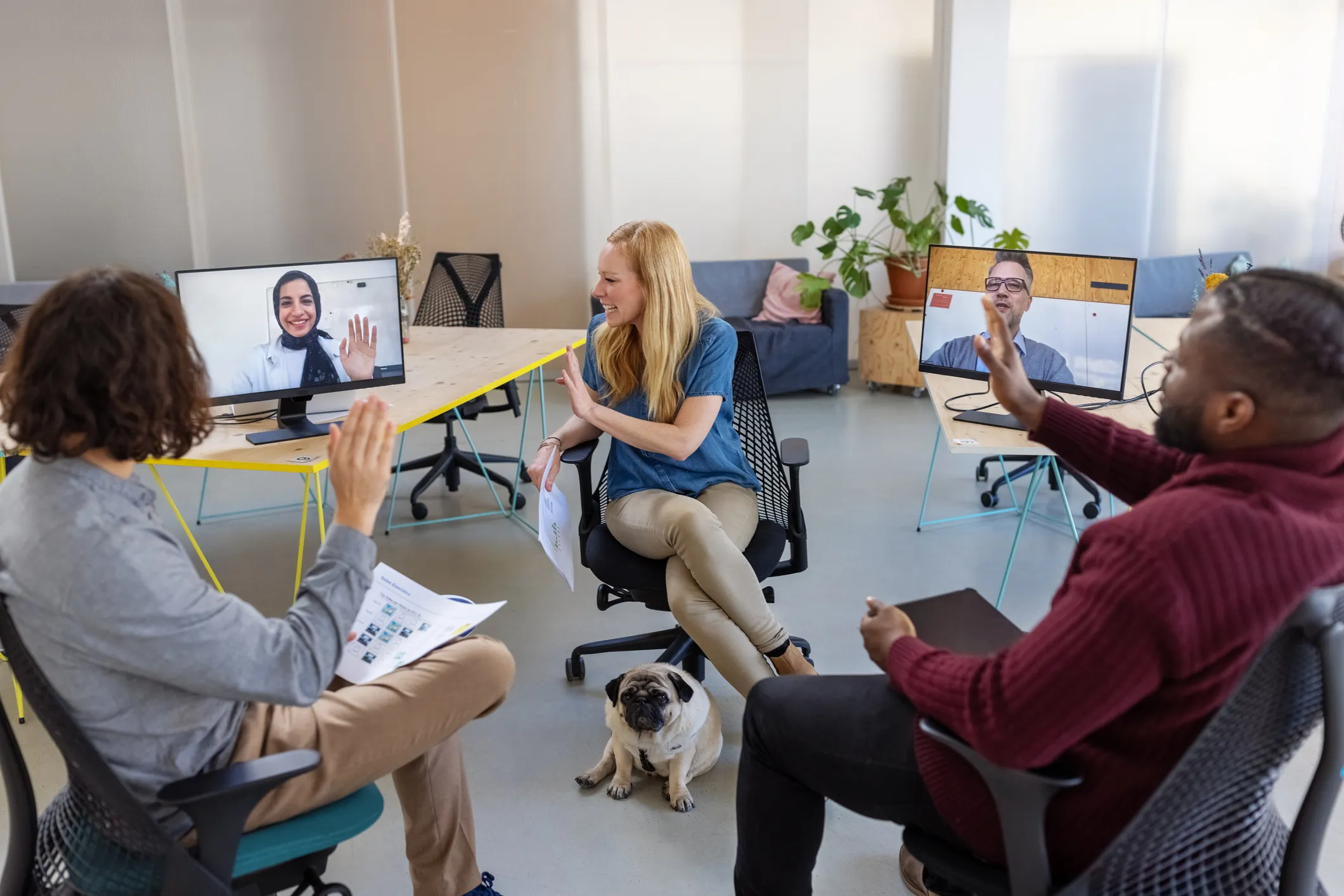 Several people gathered for a meeting, one person is joining remotely and can be seen on a monitor
