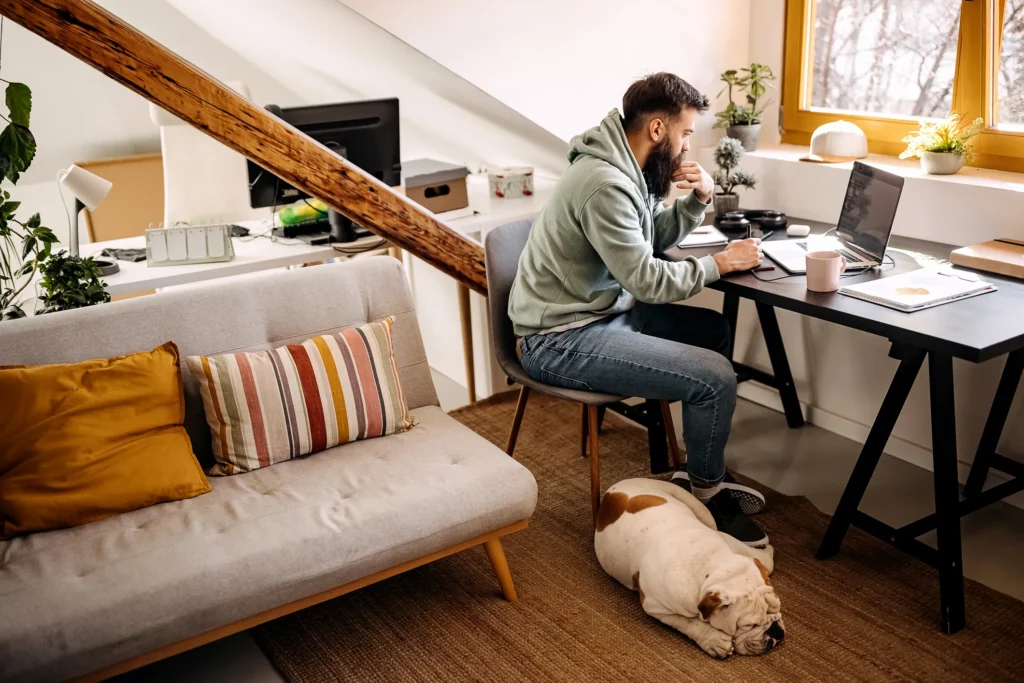 A person working at a home office, there is a bulldog sleeping on the floor.