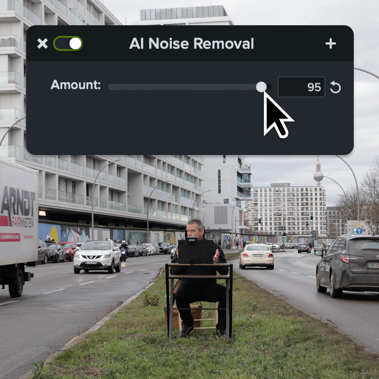 A man sitting at his desk in the middle of a traffic lane using AI noise removal to get rid of surrounding noise.